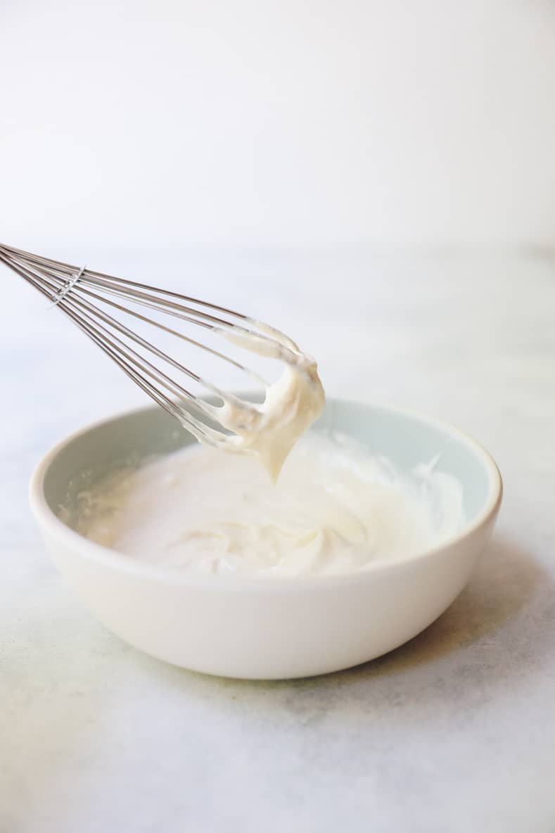 maple cream cheese frosting in a blue and white bowl with a whisk