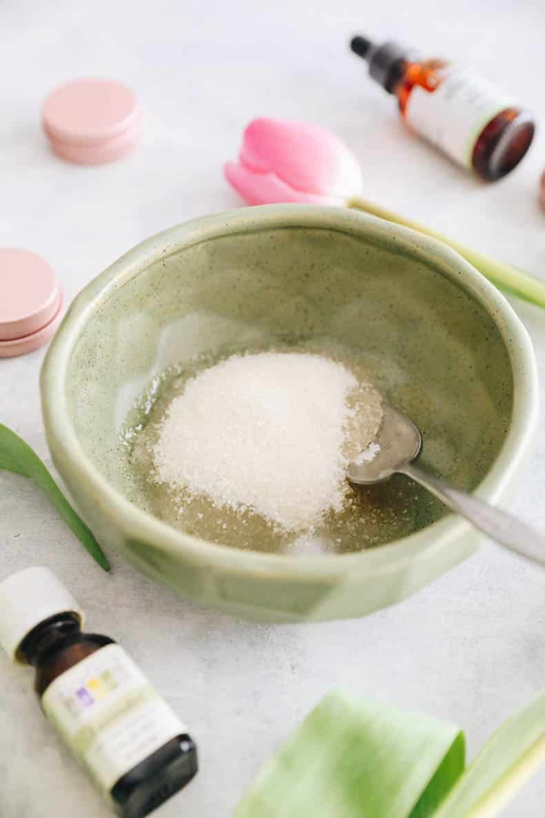 Ingredients for DIY Lip scrub in a green bowl. Sugar and coconut oil with lavender essential oil and vitamin E oil