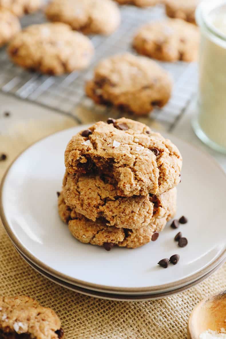 3 almond flour chocolate chip cookies stacked on a plate with a bite taken out of the top one.