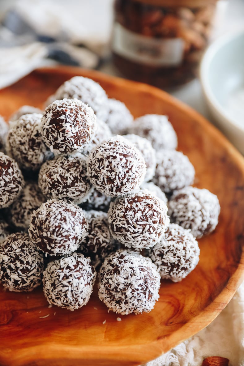 Angled shot of almond joy energy balls stacked on a wooden platter.