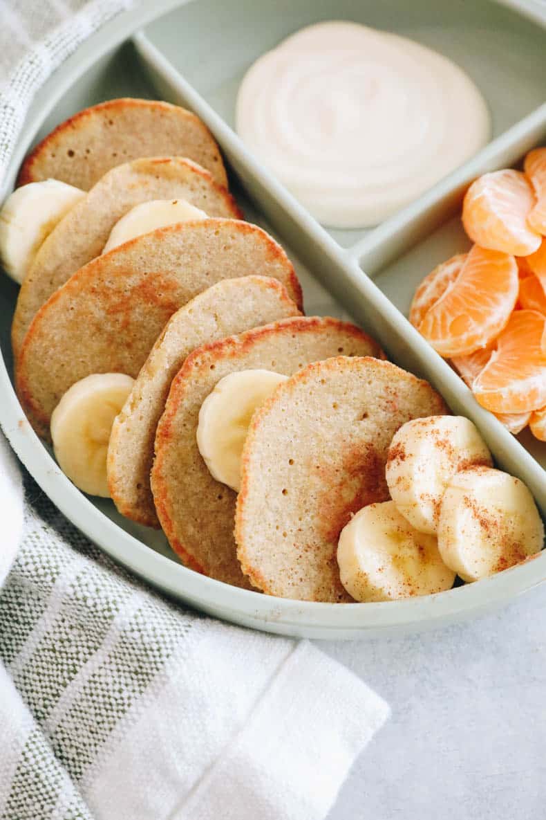 plated baby banana pancakes in a green dish with oranges and yogurt.