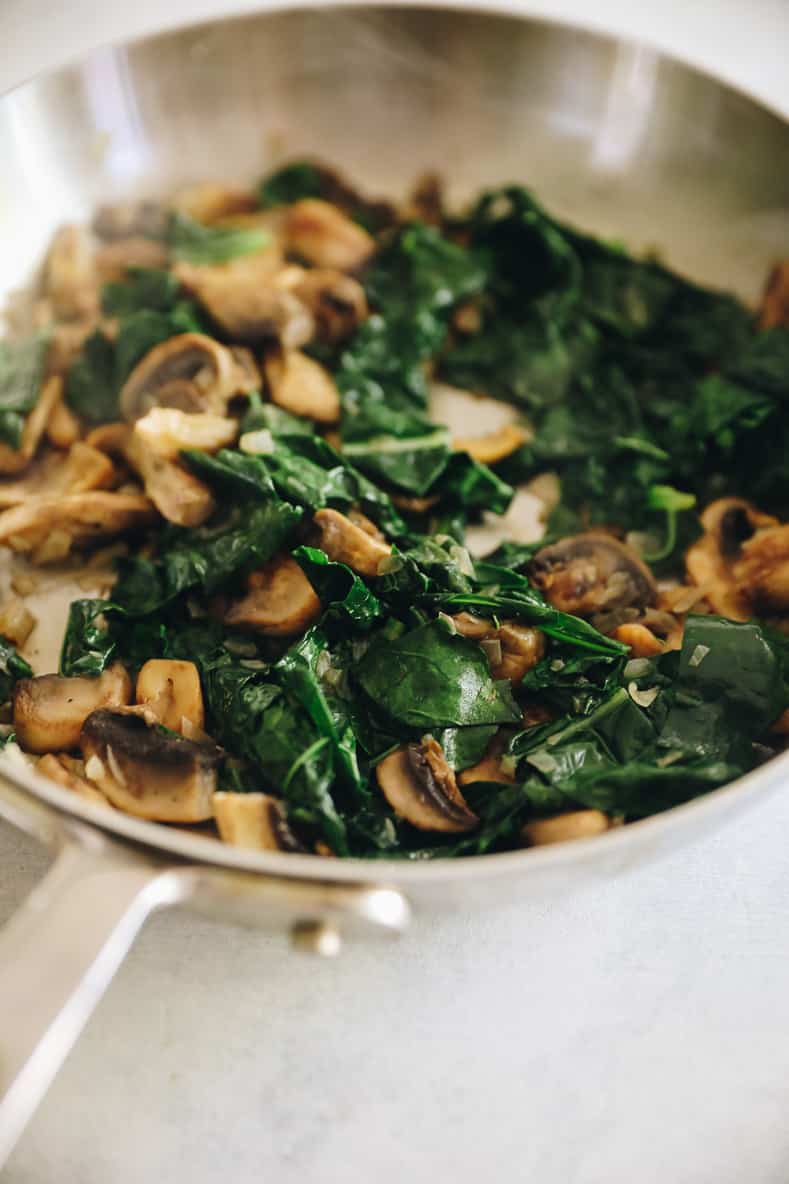 A sauté pan with mushrooms and greens.