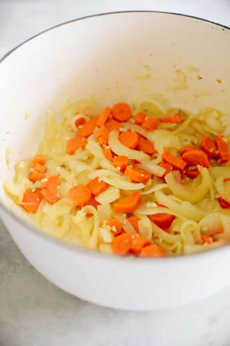 Sautéed vegetables in a large white pot.