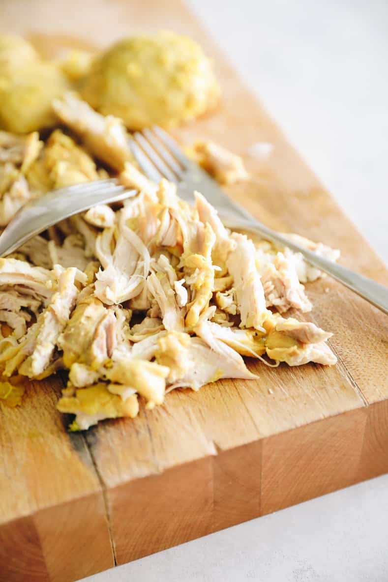 Shredded chicken with two forks on a wooden cutting board.