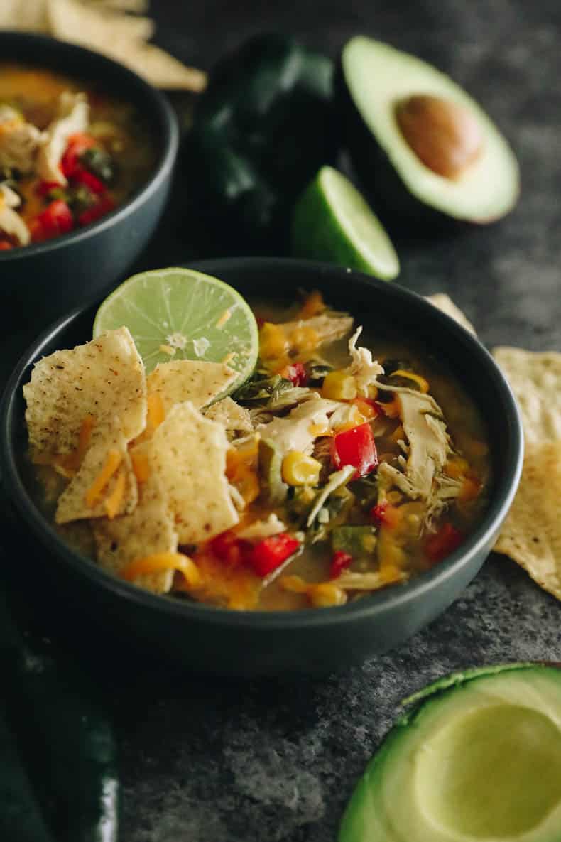 chicken poblano soup in a blue bowl with tortilla chips, lime and cheese.