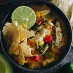 chicken poblano soup with a lime, tortilla chips and shredded cheese in a navy blue bowl.