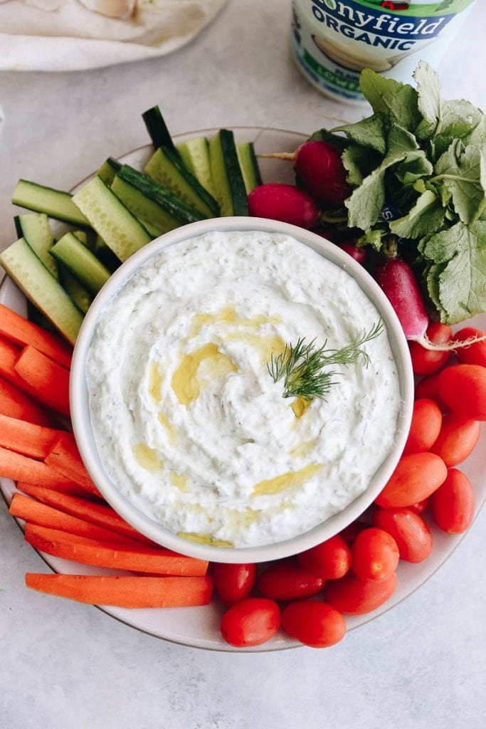 tzatziki dip in a white bowl surrounded by fresh veggies