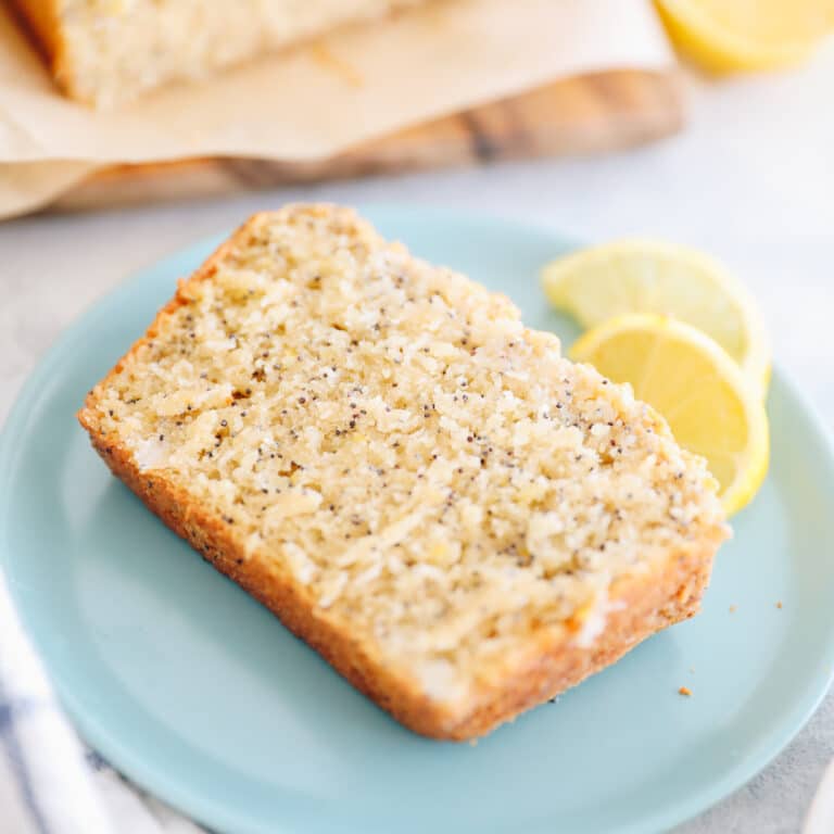 Slice of lemon poppyseed loaf on a blue plate surrounded by fresh lemon slices.