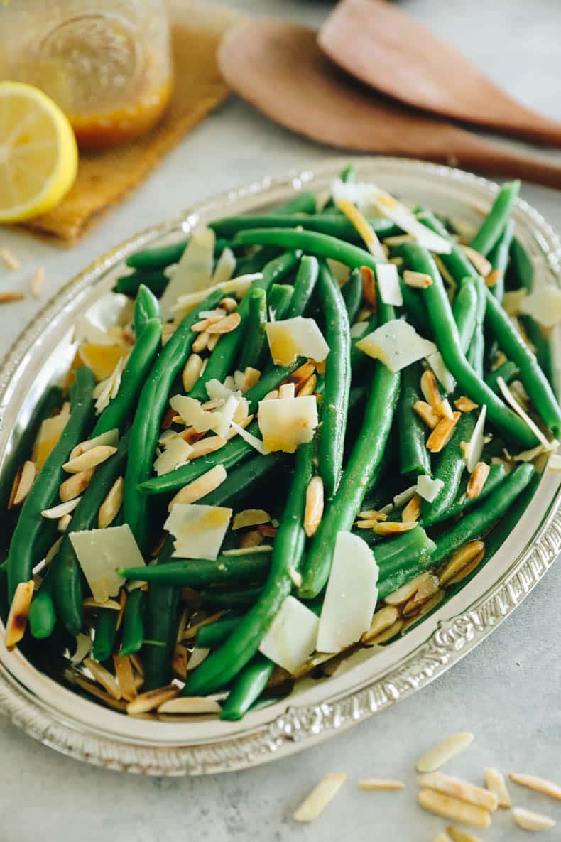 green bean salad topped with parmesan and toasted almonds on a silver platter.