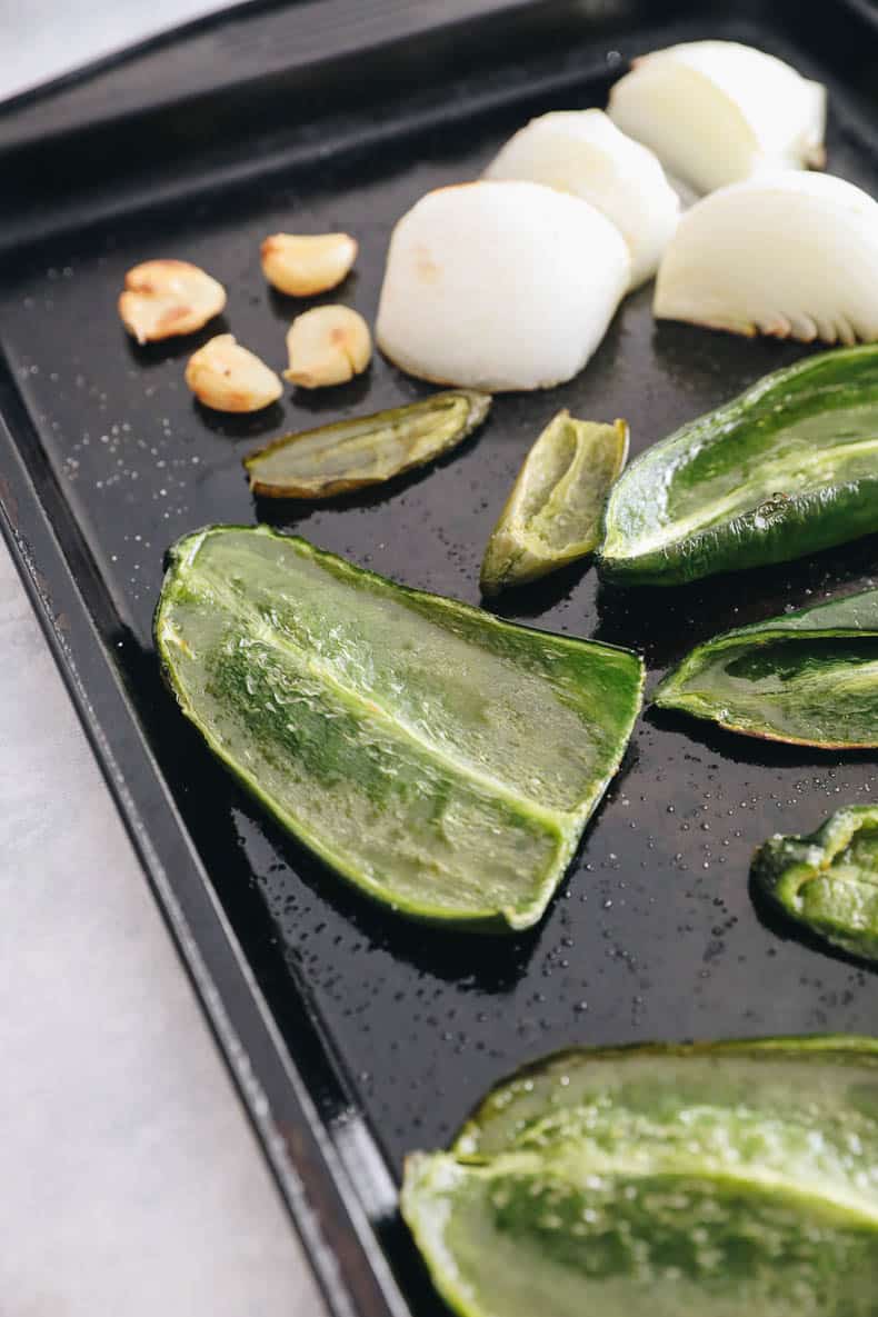 sheet pan with poblano peppers, jalapeno pepper, garlic and olive oil after being roasted.