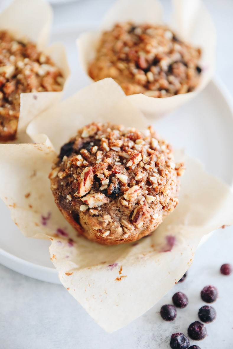 up close of blueberry oat muffins on a white plate with a paper muffin tin.