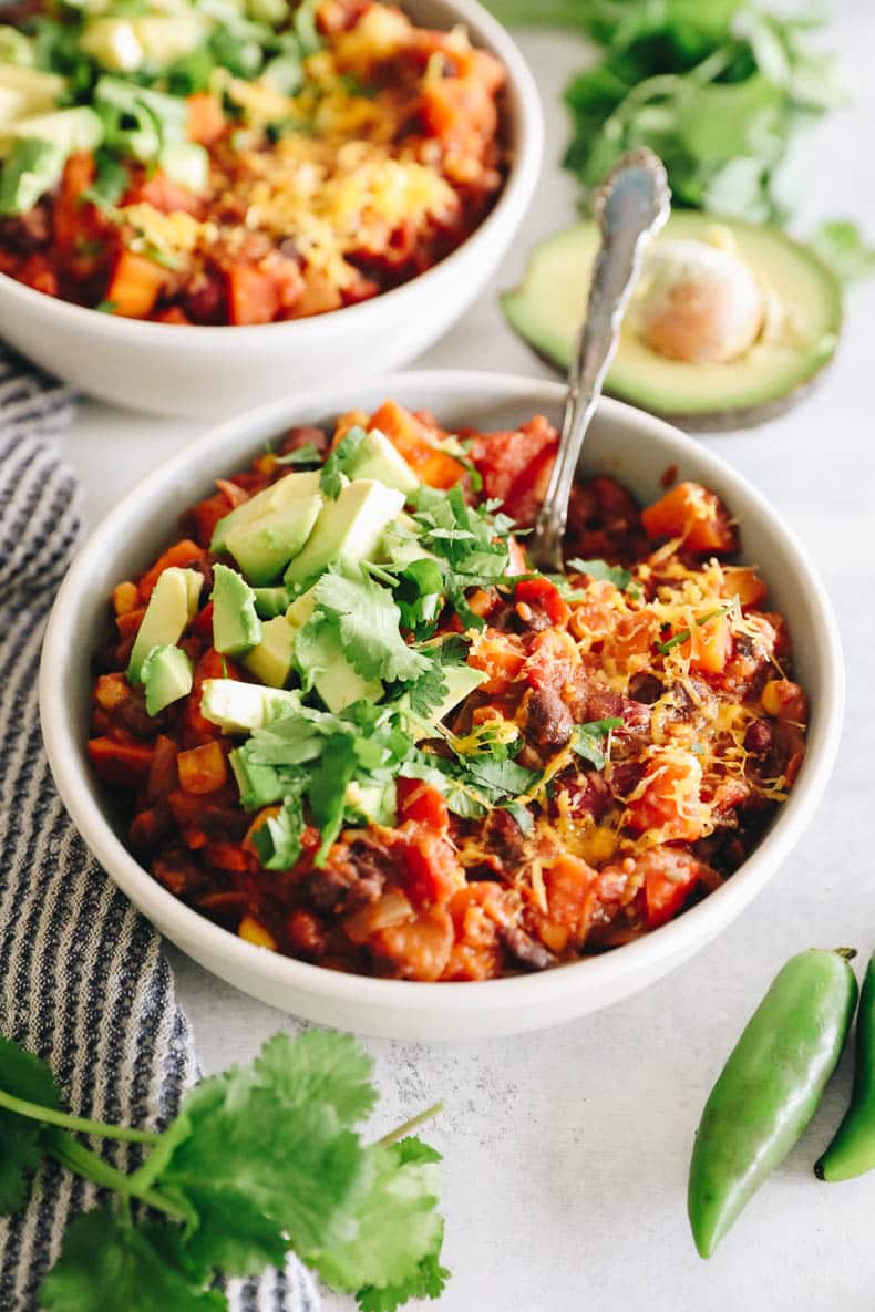 healthy veggie chili in a white bowl topped with cilantro, avocado and shredded cheese.