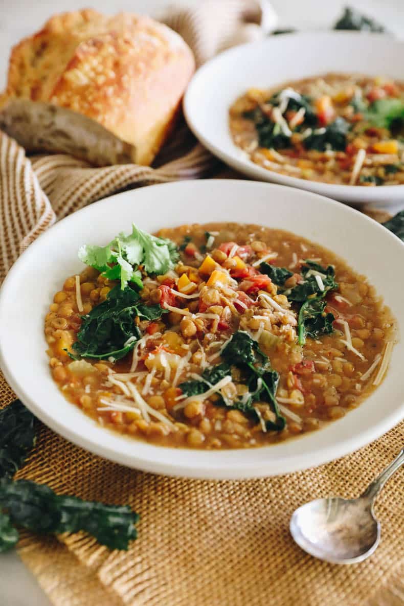 Easy lentil soup in a white bowl topped with cheese and herbs.