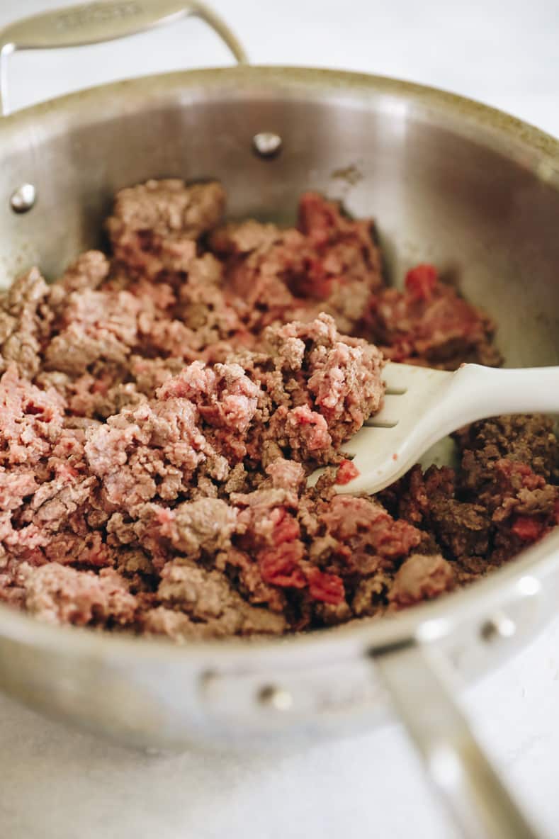 Browned meat in a sauté pan. White spatula sticking out of the pan.