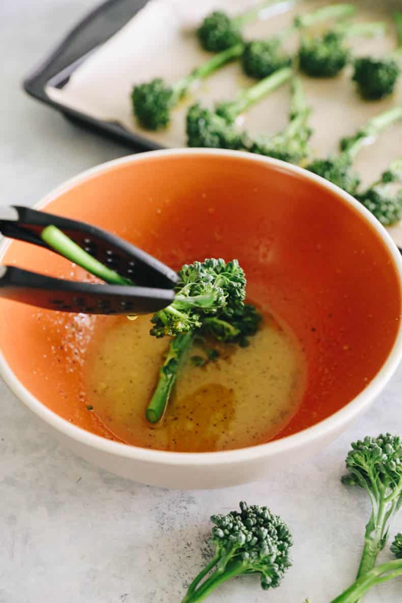 dipping raw broccolini into a bowl of lemon olive oil sauce for roasting.