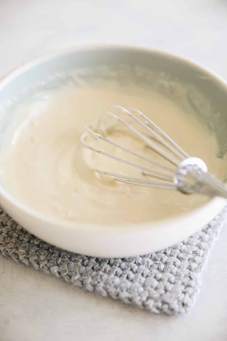 White mixing bowl with a dressing and whisk inside.