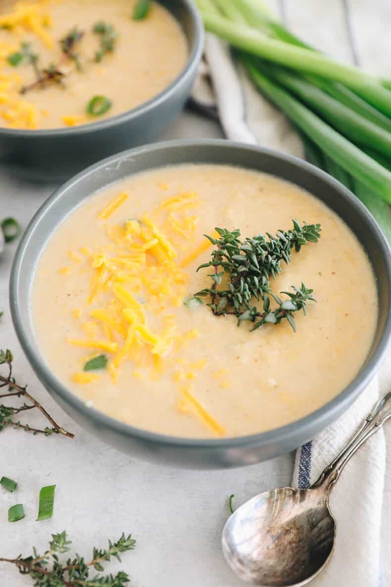 roasted cauliflower soup in a blue bowl topped with fresh thyme and cheddar cheese.