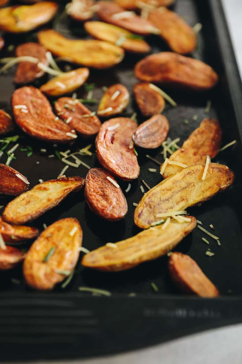 Roasted fingerling potatoes topped with rosemary and parmesan on a baking sheet