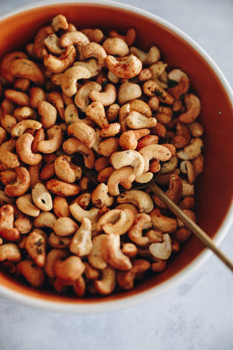 An orange bowl with spiced cashews and a gold spoon.