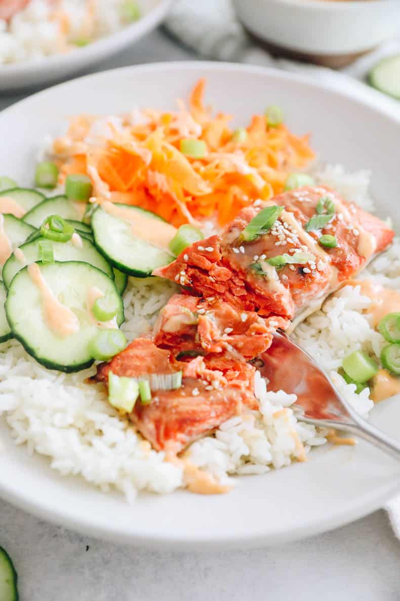 close up on a salmon bowl recipe with cooked salmon, sliced cucumbers, shredded carrots and green onions.