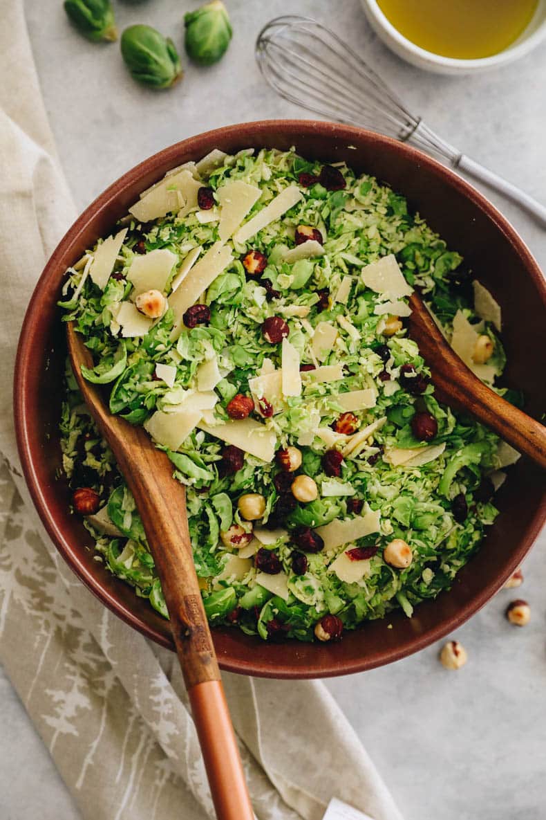 shaved brussel sprout salad in a large salad bowl with tongs.