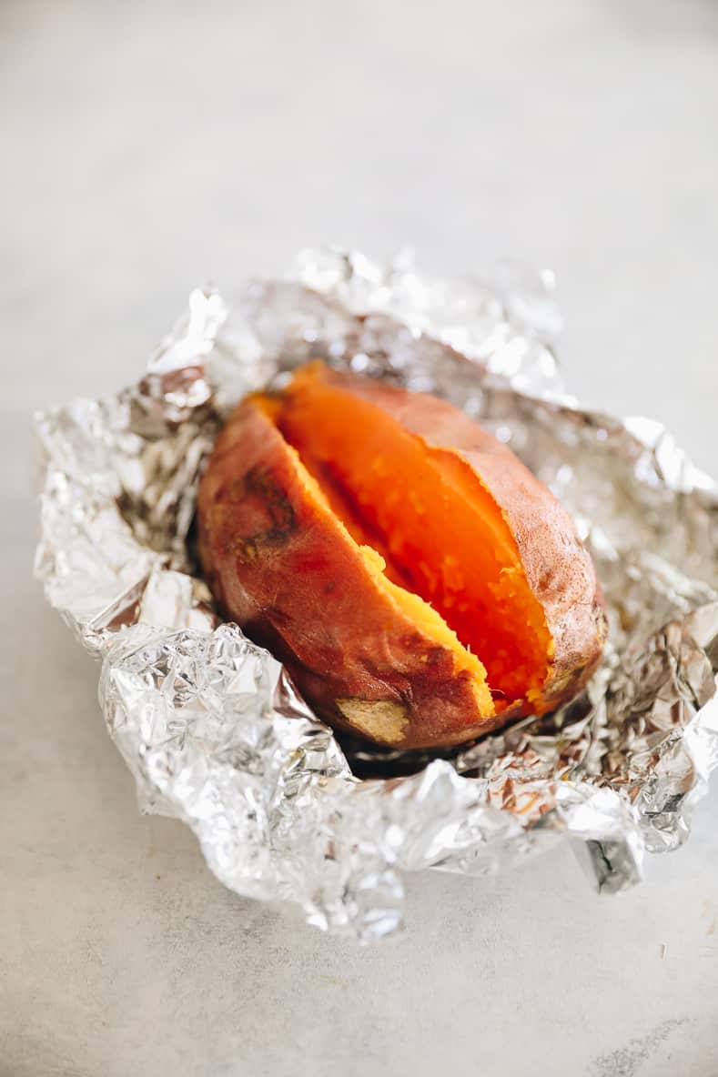 Baked sweet potato in tin foil that has been opened and sliced open.