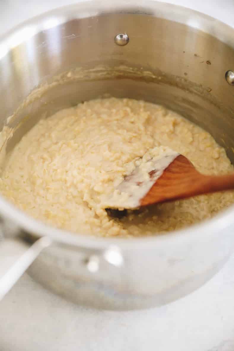 Rice pudding mixture in metal pot with wooden spoon stirring.