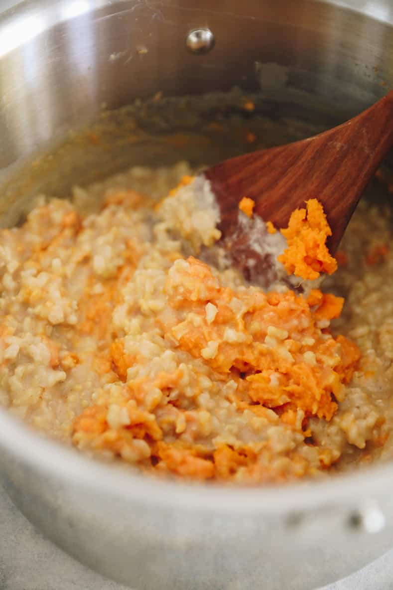 Mixture of sweet potato rice pudding in pot with wooden spoon sticking out.