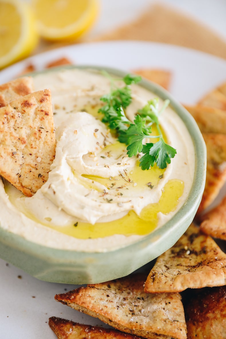 close-up image of hummus topped with olive oil, za'atar and parsley in a green bowl