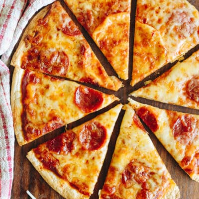 pepperoni tortilla pizza cut into slices on a cutting board.