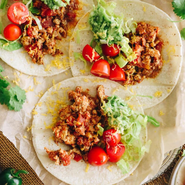 turkey tacos on white corn tortillas with ground turkey meat, tomatoes, guacamole and shredded lettuce.