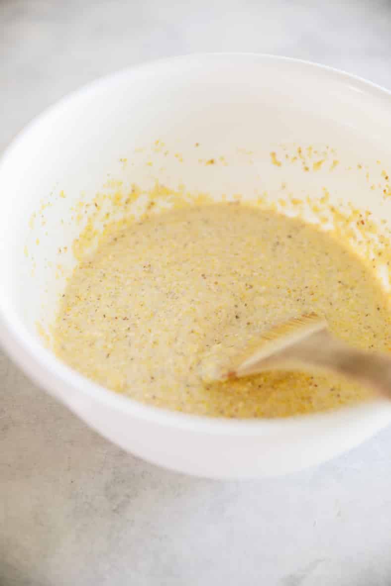 Corn pancake batter in a white mixing bowl with a wooden spoon.