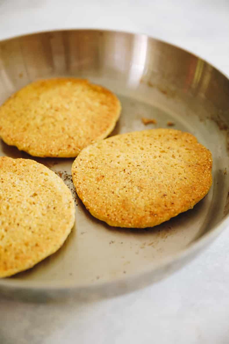 Three cooked corn pancakes in a sauté pan.