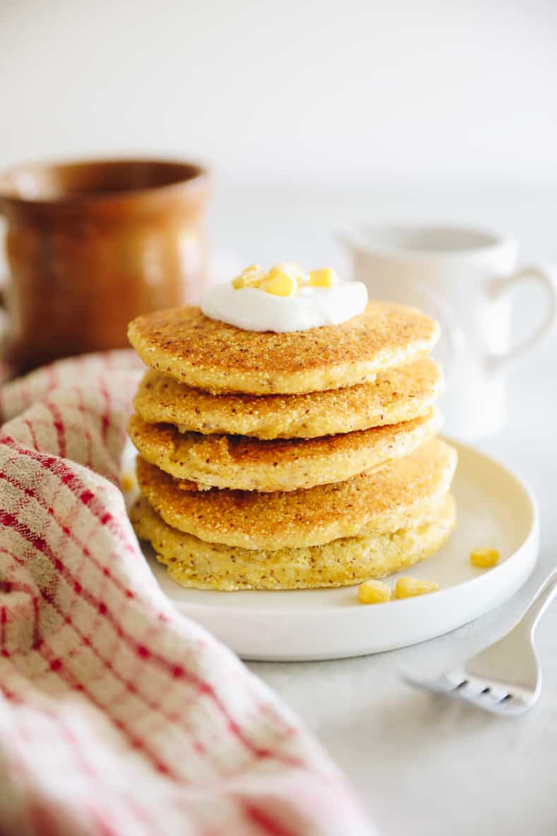 Corn pancakes stacked on a white plate and topped with a dollop of greek yogurt.