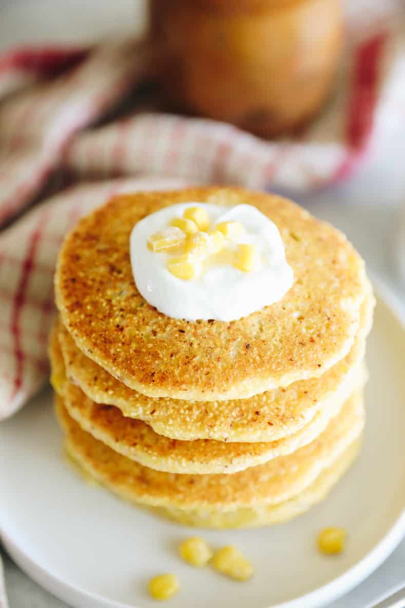 Corn pancakes stacked on a white plate and topped with a dollop of greek yogurt.