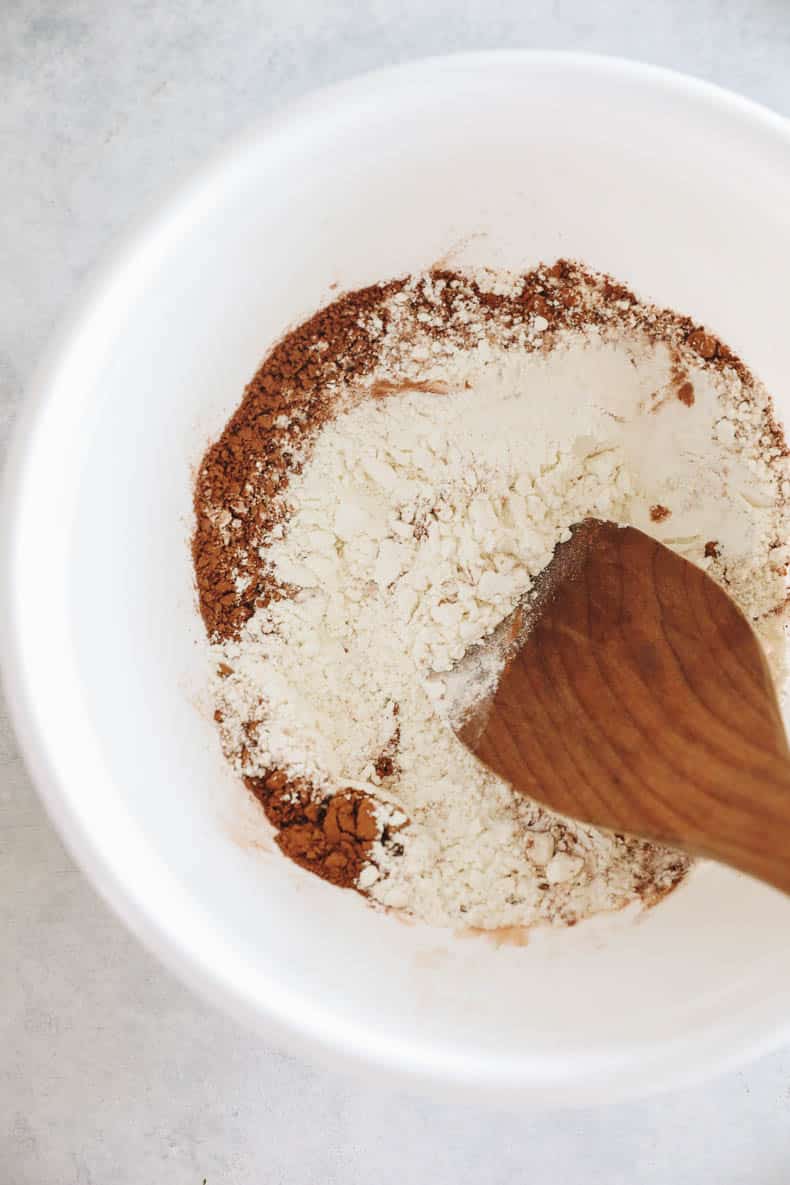 Dry ingredients for zucchini brownies in a large white mixing bowl.